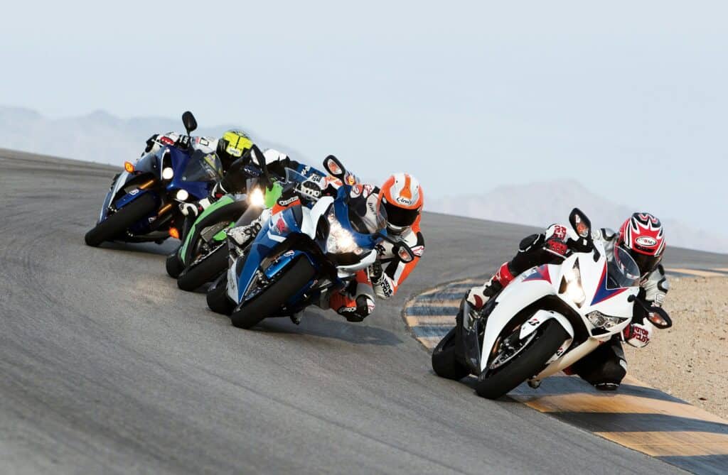 A group of people riding sports motorcycles; one of the motorcyclists is ahead of the other.