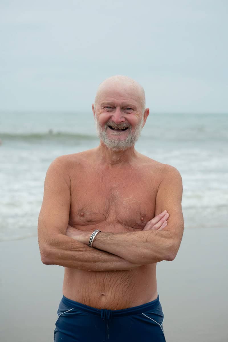 an older man standing on the beach with his arms crossed